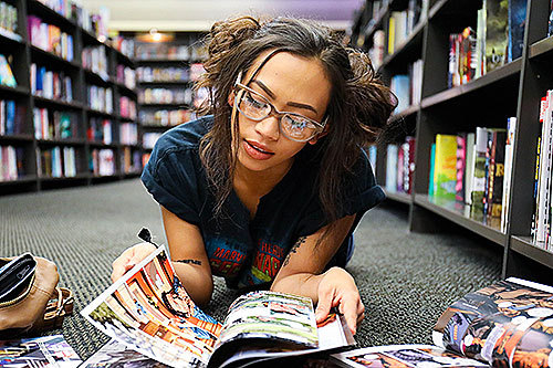 A young woman reads comics on the floor of a bookstore.