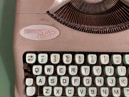 A close-up shot of a tan, Hermes Baby typewriter sitting on a table.
