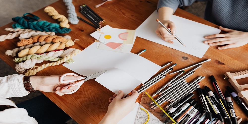People cutting paper with craft supplies surrounding them