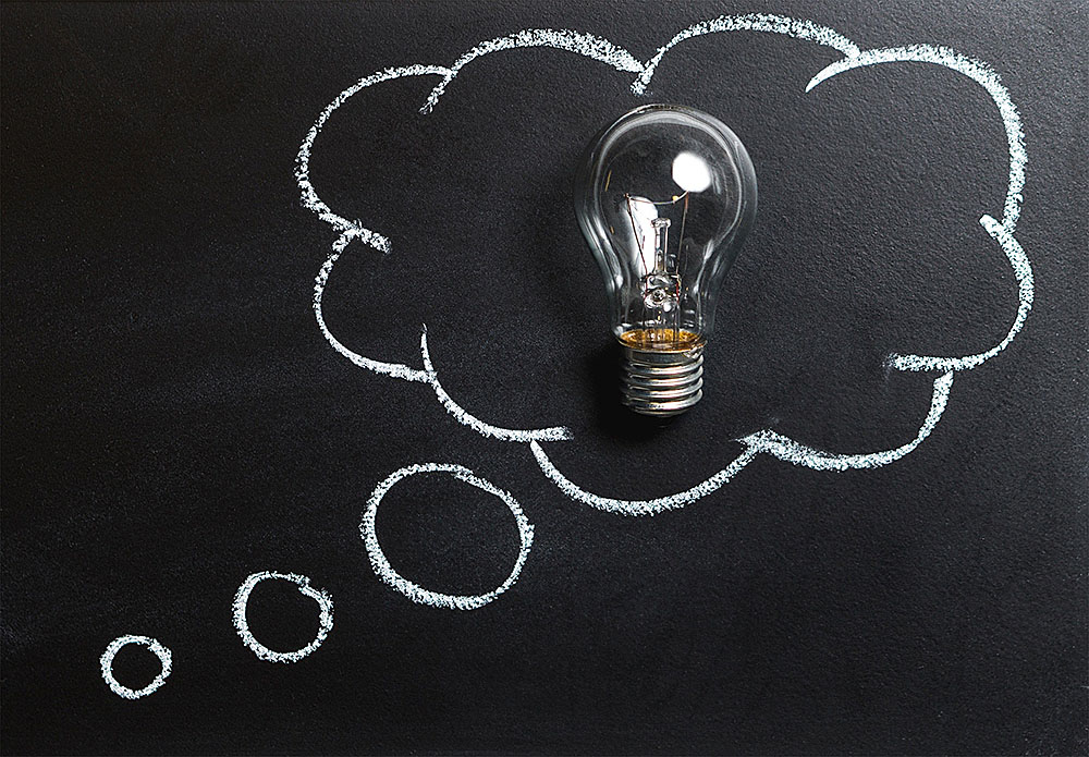 A light bulb lays on a chalkboard with a thought bubble drawn around it.