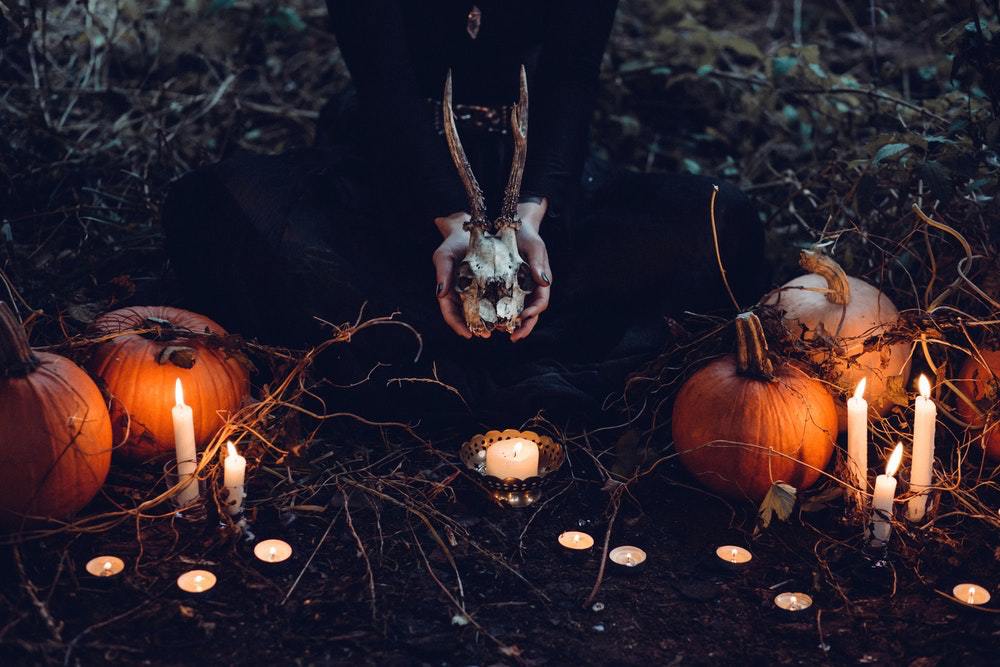 Girl_in_dark_clothes_holding_a_skull_surrounded_by_pumpkins_and_candles
