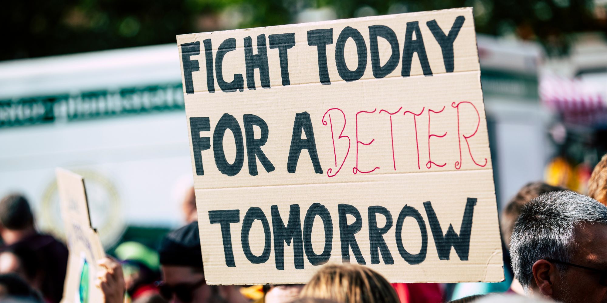 The words "fight today for a better tomorrow" written on a cardboard sign held by someone in a crowd