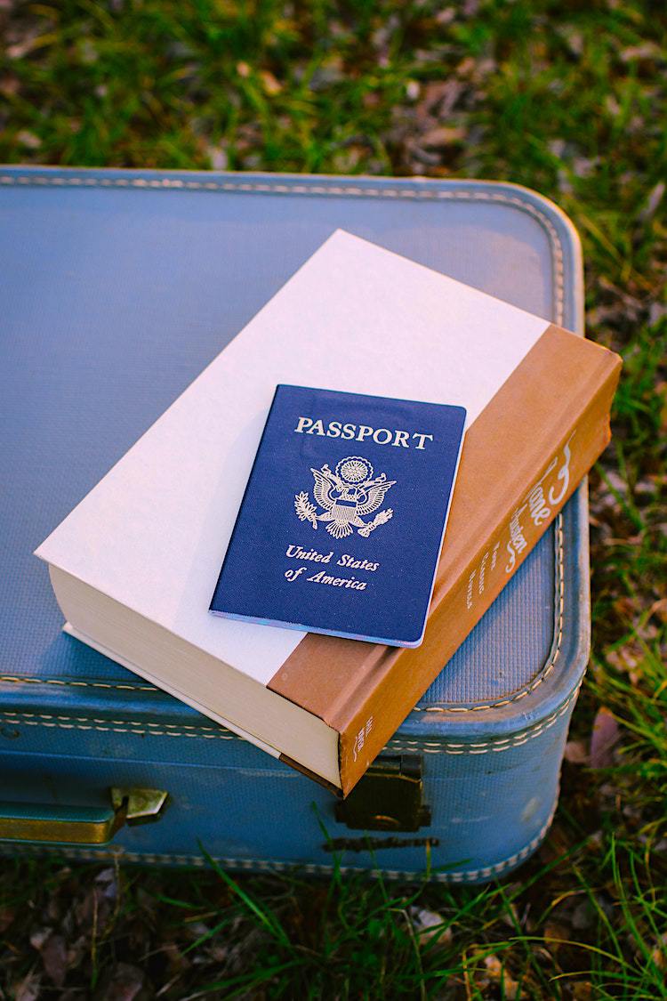 US Passport and book on top of blue suitcase