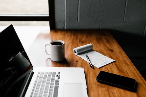 wooden desk with laptop, notepad, coffee, and smartphone