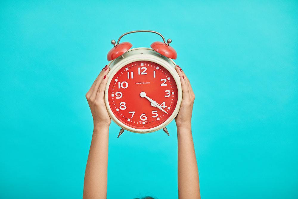Two hands holding up a red and white clock