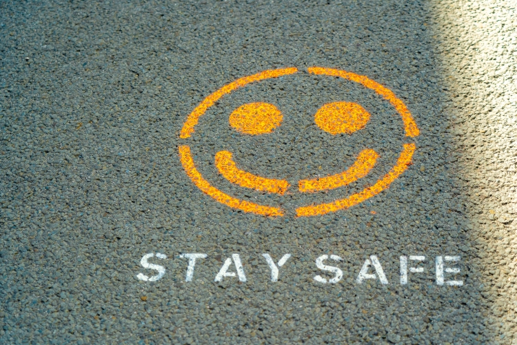 yellow smiley face painted onto pavement with text reading "stay safe"