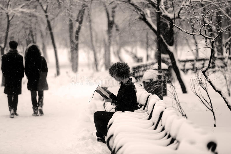 girl sitting on a park bench in snow, reading a book