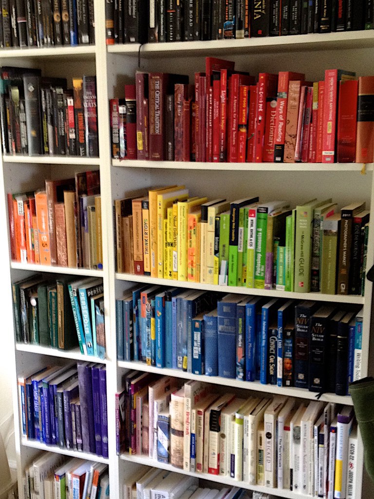 A white bookshelf filled with books organized in rainbow order