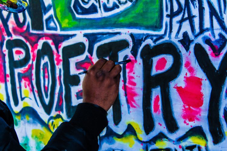 Graffiti of the word "poetry" being painted by an adult hand