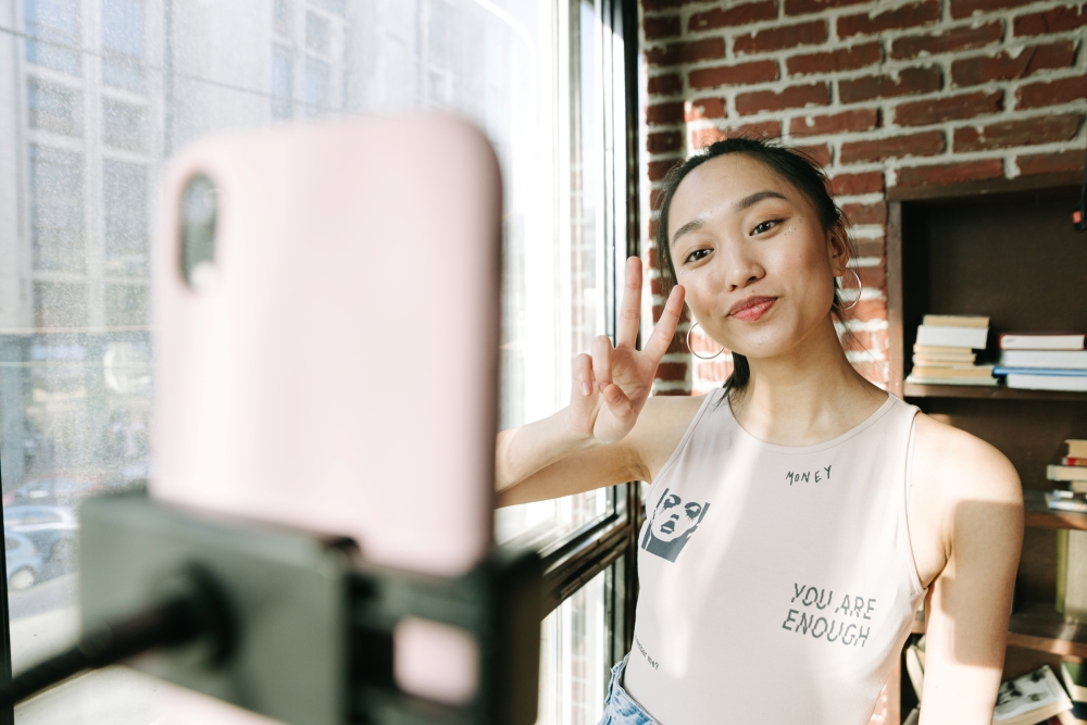 Girl making a peace sign towards her phone camera on a mount in front of her