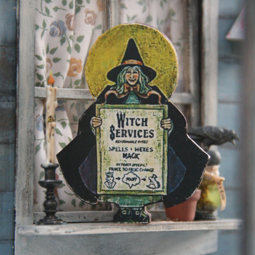 Wooden placard of a witch holding a sign on a windowsill of a house. Sign reads: "Witch services, spells, hexes, magic. October special, prince to frog change. Poof!"